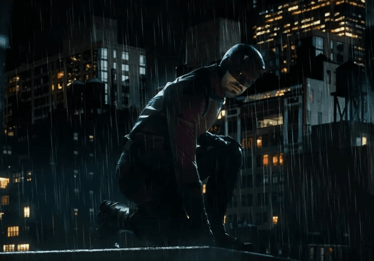 Daredevil crouching on a rooftop in the rain with the city skyline behind him at night