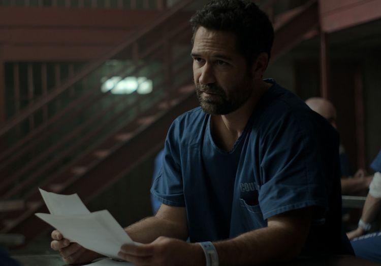 Mickey Haller in jail clothes reading a document