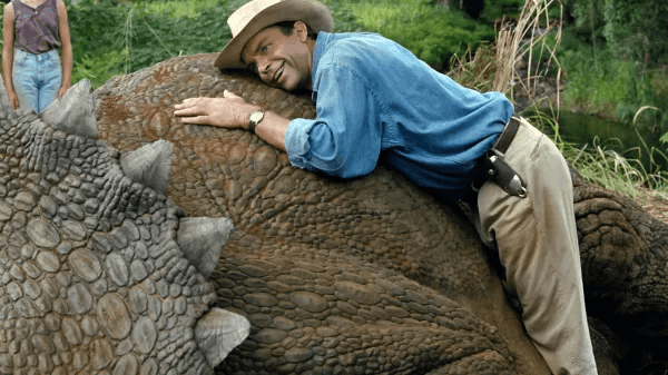 Sam Neill laughing while sleeping on a dinosaur in Jurassic Park